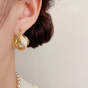 Elegant gold twisted earrings with white enamel finish shown on a model in a close-up shot