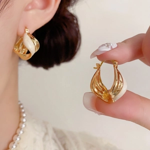 Detailed macro view of twisted gold and cream enamel hoop earrings with spiral design