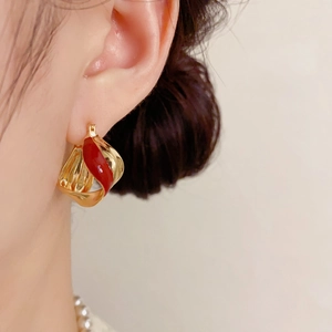 Detail view of gold twisted metal hoop earrings with red enamel on a model's ear