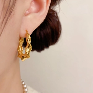 Nahaufnahme eines goldenen Wellenohrrings mit unregelmäßigem geometrischem Design