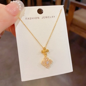 Detail shot of golden four-leaf flower pendant with sparkling cubic zirconia on white card