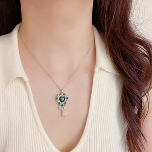 Elegante collar de corazón con gemas verdes y borlas de gotas en una modelo
