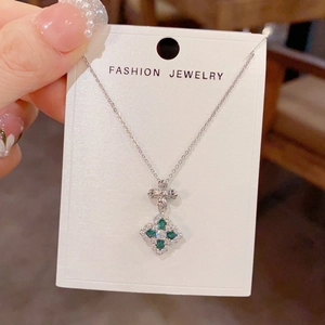 Close-up of a silver four-leaf clover pendant with green zircons on a jewelry card