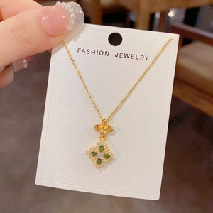 Detailed close-up of a 18K gold clover pendant with green marquise gems and white zircon