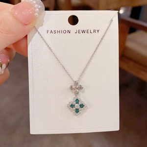 Detail of silver clover pendant necklace with green gemstones and sparkling bow design