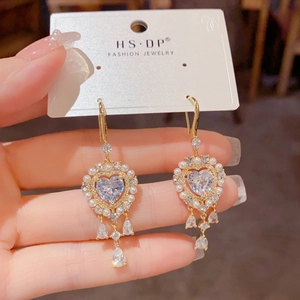 Detalle de pendientes de corazón dorado con borde de perlas y borlas de circón en gota