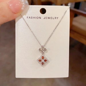 Close-up of a silver four-leaf flower pendant necklace with red and white gemstones