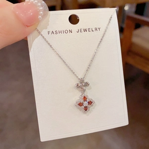 Detail of silver clover pendant necklace with orange gems and bow knot on a display card