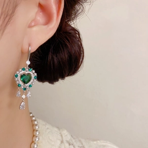 Detalle de pendientes vintage plateados con corazón verde y flecos de gota en modelo