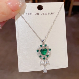 Detalle de collar corazón vintage con piedra verde esmeralda, perlas y borlas de gotas