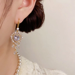 Detalle de pendientes dorados con circonita de corazón, perlas y cristales finos