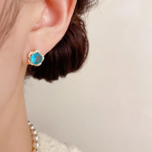 Détail d'une boucle d'oreille fleur en zircon bleu portée par un mannequin élégant