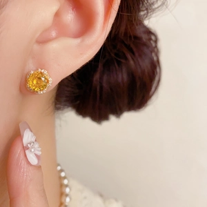 Gros plan de boucles d'oreilles fleur en or avec pierre jaune sur le lobe d'oreille