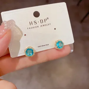Détail de puce d'oreille fleur dorée avec zircon bleu et tige en argent S925