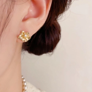 Minimalistische goldene Blütenohrstecker mit Zirkon auf dem Ohrläppchen des Models