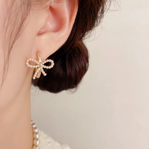 Primer plano de pendientes de lazo con perlas y diamantes en base dorada