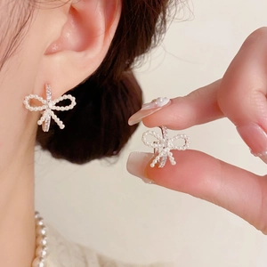Detalle de pendientes de lazo con perlas y pedrería en la oreja y en la mano