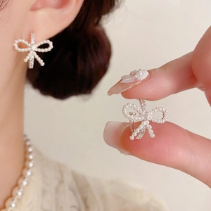 Detalle de pendientes de lazo plateados con perlas y circones en una modelo