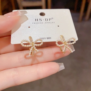 Detalle de pendientes de lazo dorado con perlas blancas y agujas de plata S925