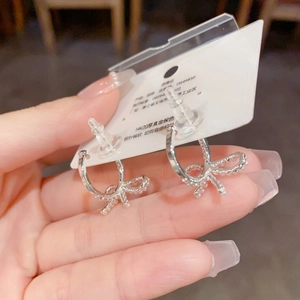 Detalle de pendientes de lazo plateados con perlas blancas en tarjeta de exhibición