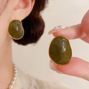 Detail of dark green irregular enamel stud earrings with gold trim worn by a model