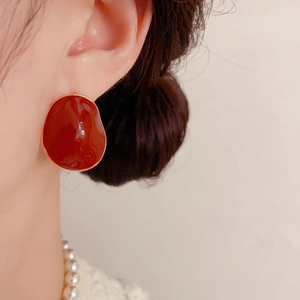 Close-up of irregular red enamel earrings with gold trim worn by a model