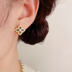 Gros plan d'une boucle d'oreille en or avec pétales de trèfle vert et zircons brillants