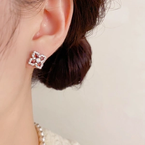 Détail de boucles d'oreilles trèfle en argent avec cristal rouge portées par le mannequin