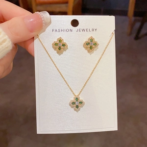 Détail d'une parure de bijoux trèfle doré avec zircons verts et blancs sur carte cadeau