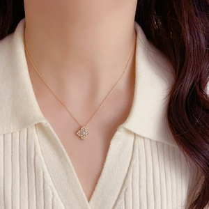 Vue détaillée d'un collier trèfle doré avec zircons porté sur un pull en maille blanc