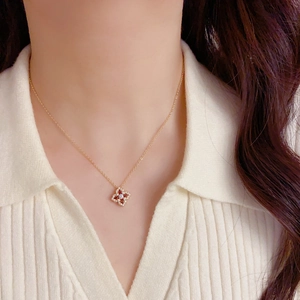 Détail d'un collier trèfle doré serti de zircons rouges et blancs porté par un mannequin