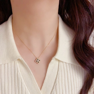 Détail d'un collier pendentif trèfle en zircon noir porté sur une chemise blanche texturée