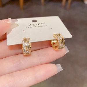 Détail de boucles d'oreilles étoile dorées avec zircons pavés et motif étoilé en relief