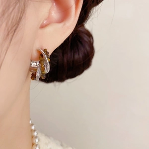 Detail einer silbernen Perlenohrring-Creole am Ohr mit braunem Tigerauge und Spiralstruktur