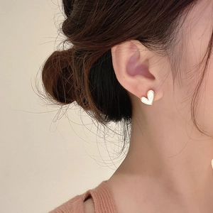 Elegant gold heart stud earrings with white pearl texture worn by a model