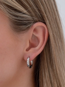 Gros plan d'une boucle d'oreille créole argentée portée par un mannequin de profil