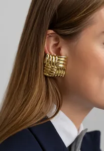 Close-up of golden square earrings with textured weave design worn by a model