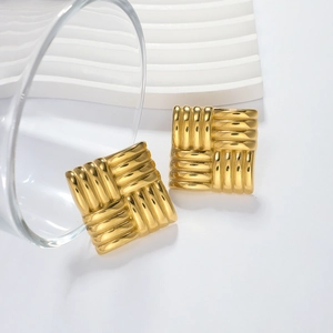 Exaggerated golden square earrings with textured woven metal surface on a white display