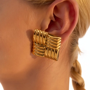 Macro shot of large square gold earrings with woven texture on a female model's ear