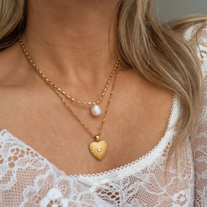 Detail einer goldenen Schichtkette mit Naturperle und graviertem Herzanhänger am Hals