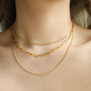 Close-up of triple-layered 18K gold-plated paperclip and link chain necklaces on a model