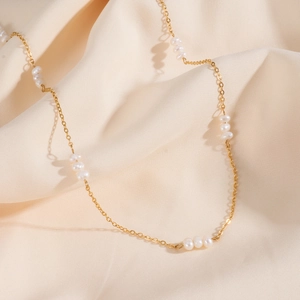 Détail d'un collier en acier inoxydable doré 18K avec petites perles d'eau douce sur satin