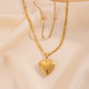 Dettaglio di collana dorata a strati con medaglione a cuore, catena figaro e perla bianca