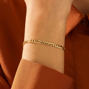 Λεπτομέρεια από επιχρυσωμένο βραχιόλι Figaro 18K πάνω σε πορτοκαλί σατέν μανίκι