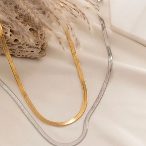 Detail of 3mm gold and silver flat snake bone chains on a natural textured stone background