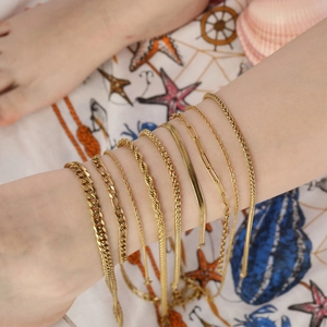 Detail of multi-layered 18K gold plated Figaro and Cuban link anklets set on a beach background
