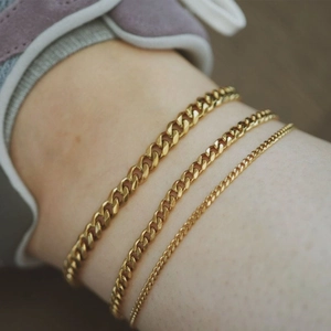 Close-up of three layered 18K gold plated Cuban link anklets on a woman's ankle