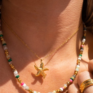 Gold starfish pendant layered with colorful beaded necklace on model for summer