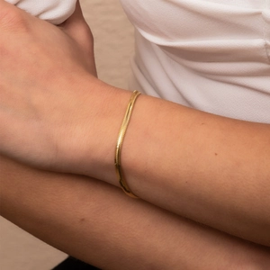 Detailopname van een glanzende 18K vergulde platte slangenketting armband om een vrouwelijke pols