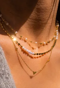 Gros plan d'un collier triple épaisseur avec perles et pendentif cœur doré sur modèle